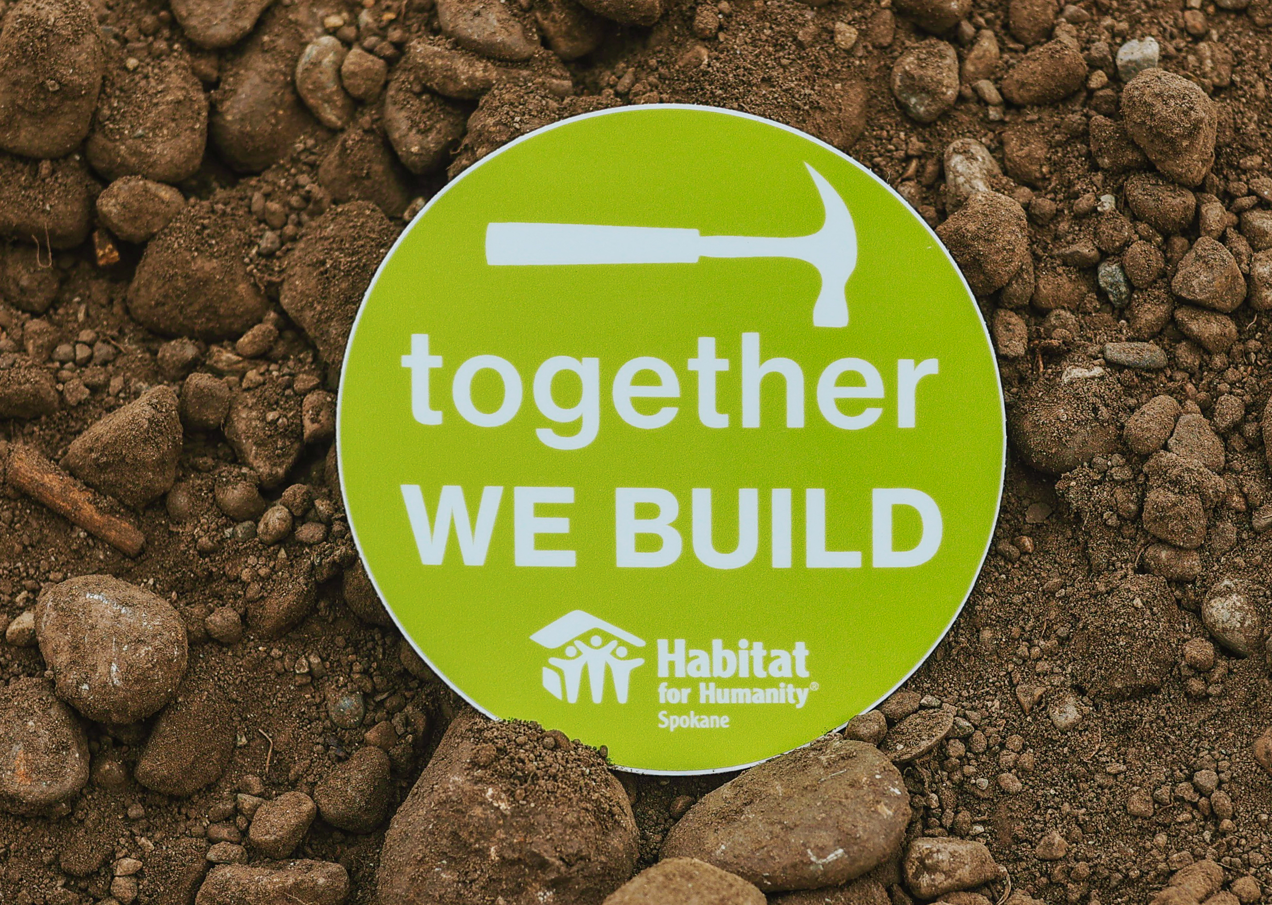 Photo of a green sticker on dirt saying together we build with a hammer icon above it. Credit: @Bex_Effect | @bexeffect